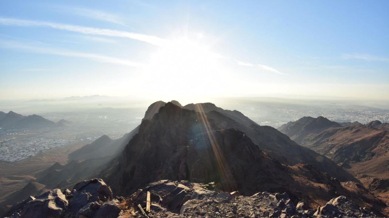 Intercontinental Dar Al Iman Madinah By Ihg Hotel Medina Exterior foto The photo shows a scenic view from a mountain top, with peaks silhouetted against the bright sun. The sun is positioned low in the sky, creating a warm glow and illuminating the landscape below. In the foreground, there are rocky terrains, while the 