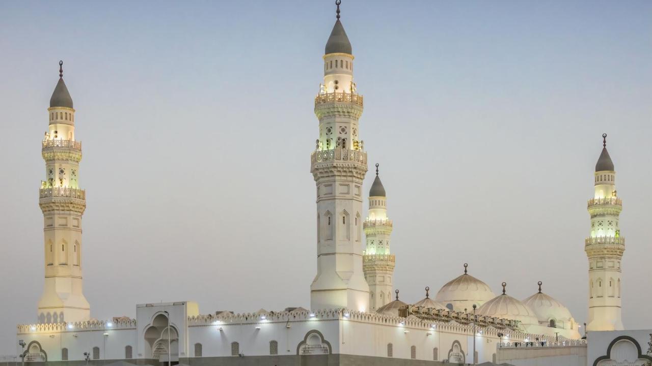 Intercontinental Dar Al Iman Madinah By Ihg Hotel Medina Exterior foto The image shows a mosque with distinct architectural features, including tall minarets and domes. The minarets are highlighted, likely lit up in the evening, showcasing intricate design elements typical of Islamic architecture. The overall scene conv