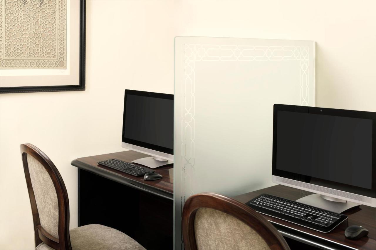 Intercontinental Dar Al Iman Madinah By Ihg Hotel Medina Exterior foto The photo shows a workspace featuring two computers set up on a dark wooden desk. Each computer has a monitor and a keyboard. A frosted glass partition is placed between the two workstations, providing some privacy. In the background, there is a fram