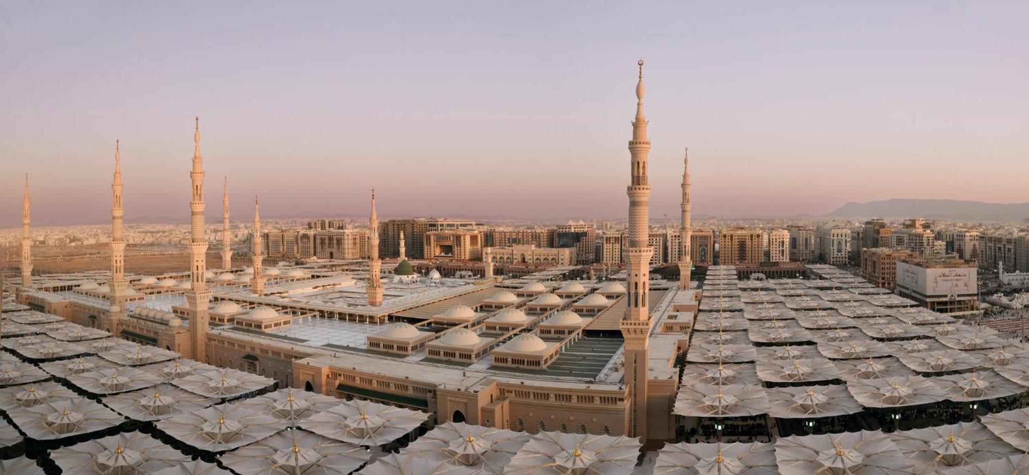 Intercontinental Dar Al Iman Madinah By Ihg Hotel Medina Exterior foto The photo shows an aerial view of the Al-Masjid an-Nabawi, or the Prophet's Mosque, located in Medina, Saudi Arabia. The mosque features distinct minarets, large white domes, and expansive open areas with large umbrellas that provide shade for visito