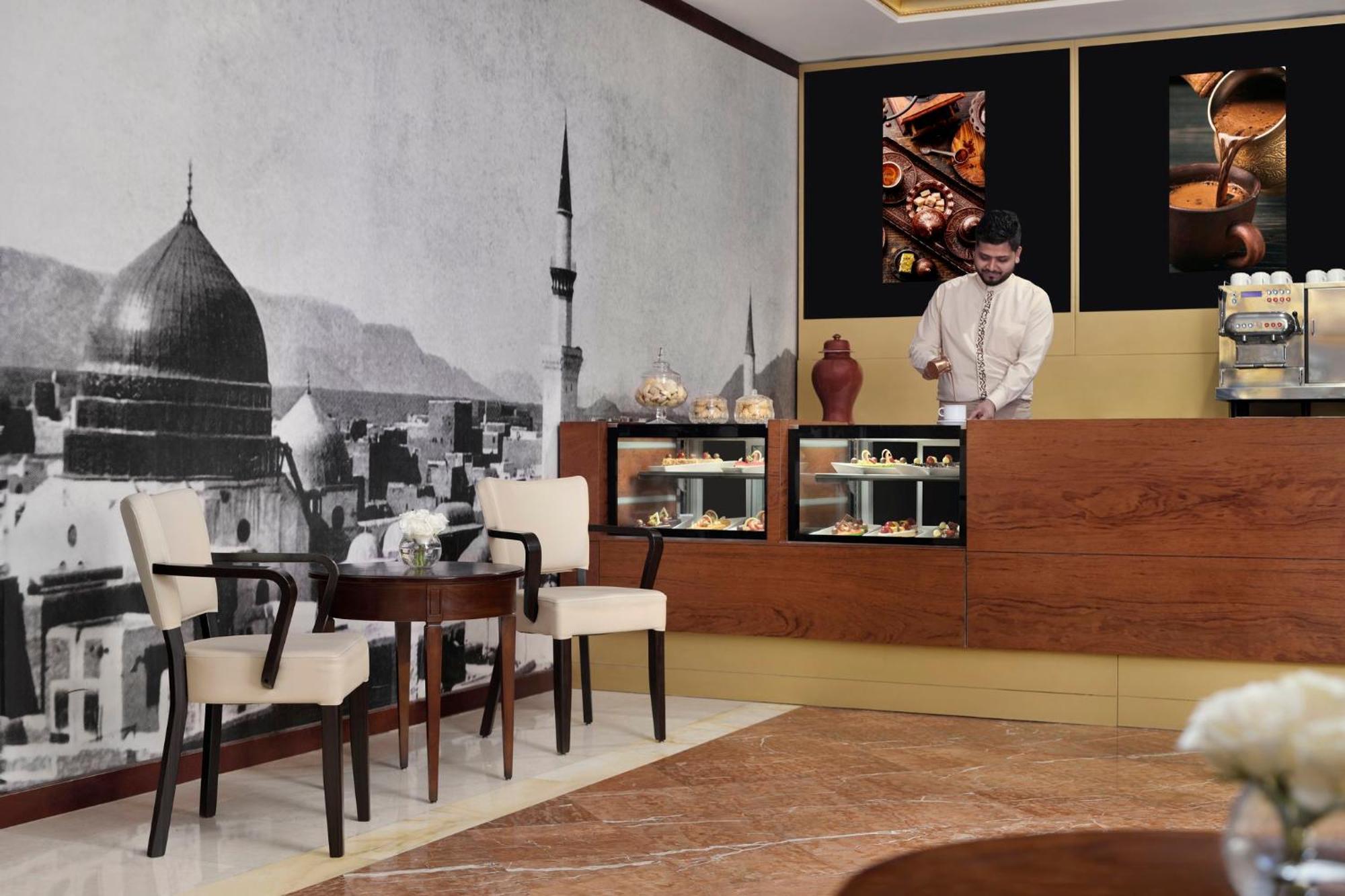 Intercontinental Dar Al Iman Madinah By Ihg Hotel Medina Exterior foto The photo shows a stylish interior of a café or pastry shop. In the background, there is a large black-and-white mural depicting a cityscape, featuring a prominent dome and minaret, suggesting an architectural style that could be from a Middle Easter