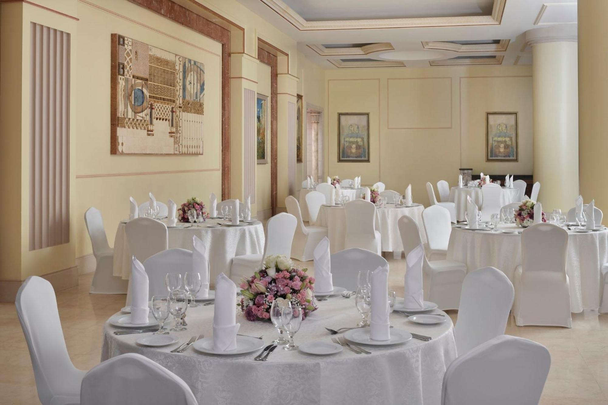 Intercontinental Dar Al Iman Madinah By Ihg Hotel Medina Exterior foto The photo shows an elegantly arranged dining or function room. There are round tables covered with white tablecloths, each set with fine dining ware including glassware, utensils, and neatly folded white napkins. Some tables have floral centerpieces 
