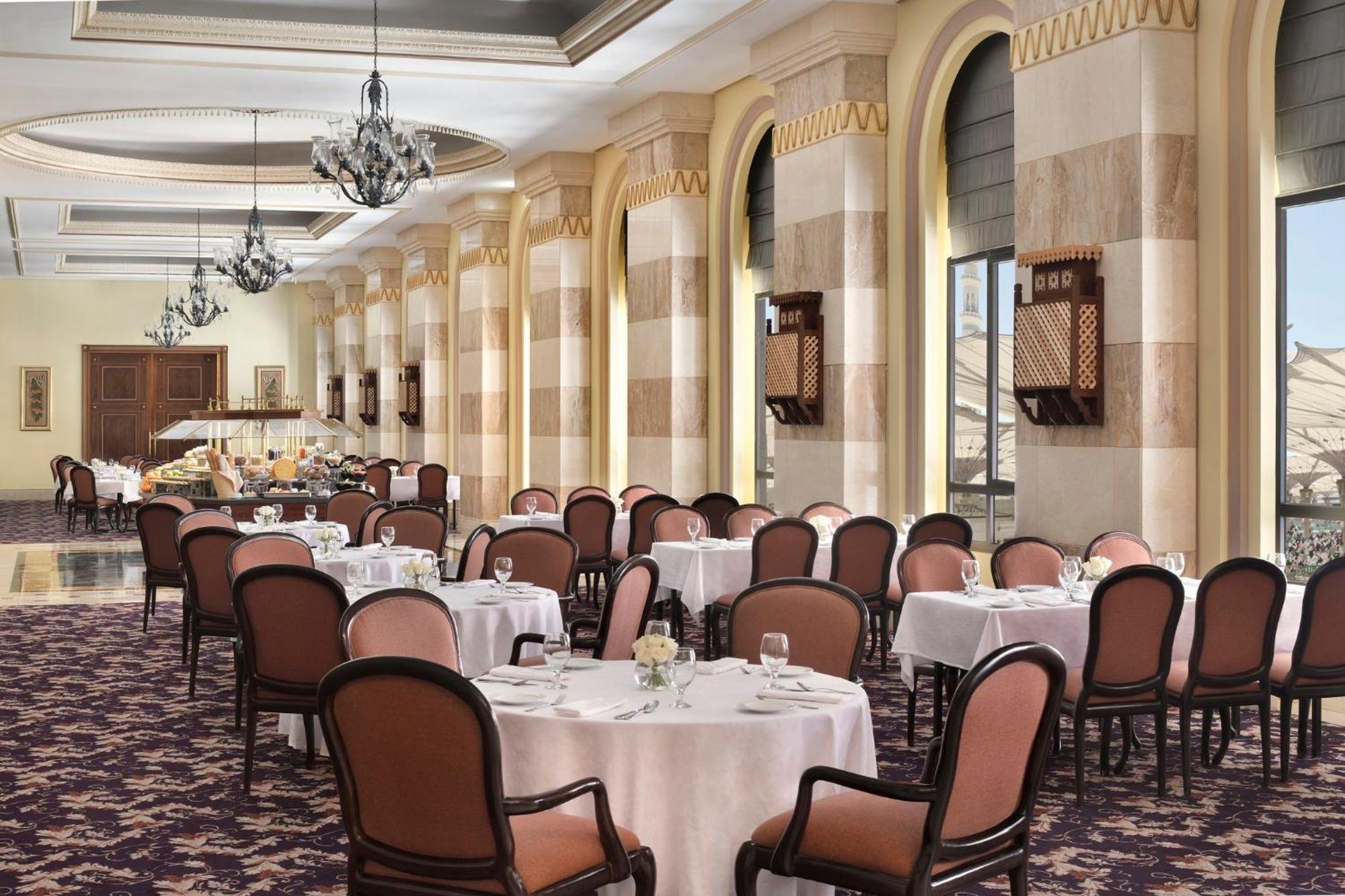Intercontinental Dar Al Iman Madinah By Ihg Hotel Medina Exterior foto The photo depicts an elegant dining room setting. It features several round tables covered with white tablecloths, each set with dishes and glassware. The room has a sophisticated ambiance, characterized by high ceilings adorned with chandeliers and 