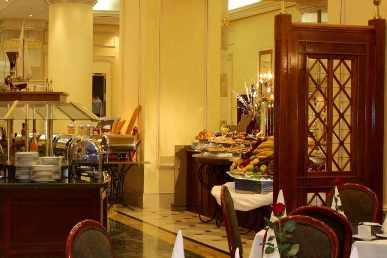 Intercontinental Dar Al Iman Madinah By Ihg Hotel Medina Exterior foto The photo shows an elegant dining area, likely within a restaurant or a hotel. There's a buffet setup on one side with various food items displayed, including pastries and fruits. The room features warm lighting, polished floors, and decorative walls